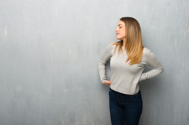 Jonge vrouw op getextureerde muur lijden aan rugpijn voor het hebben van een inspanning