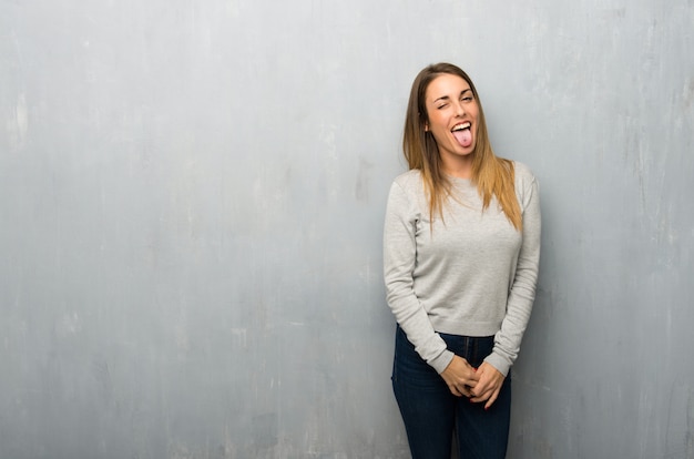 Jonge vrouw op geweven muur die tong toont bij de camera die grappige blik hebben