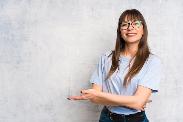 Jonge vrouw op grungeachtergrond die handen uitbreiden aan de kant voor het uitnodigen om te komen