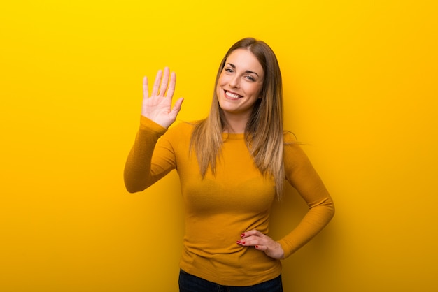 Jonge vrouw op het gele achtergrond groeten met hand met gelukkige uitdrukking