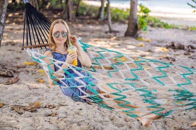 Jonge vrouw op het strand in een hangmat met een drankje