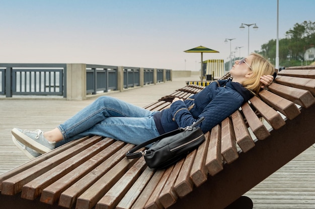Jonge vrouw op lege stadsdijk rust met haar ogen gesloten op een ligstoel