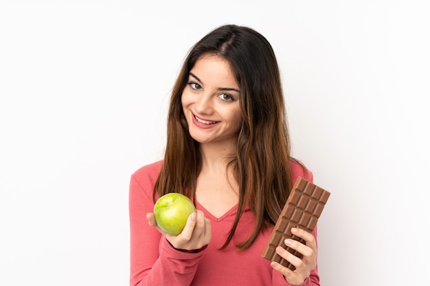 Jonge vrouw op roze met een chocoladetablet in de ene hand en een appel in de andere