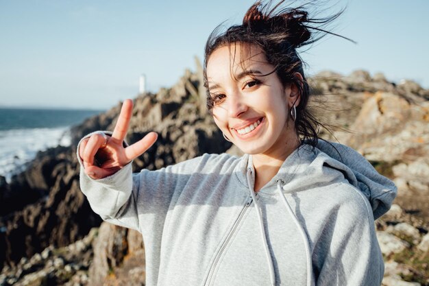 Jonge vrouw op sportkleding die het overwinningsteken met de hand naar de camera doet na training buitenshuis Gemoedsrust concept Aan de kust tijdens een zonnige dag winderige en natuurlijke ambient