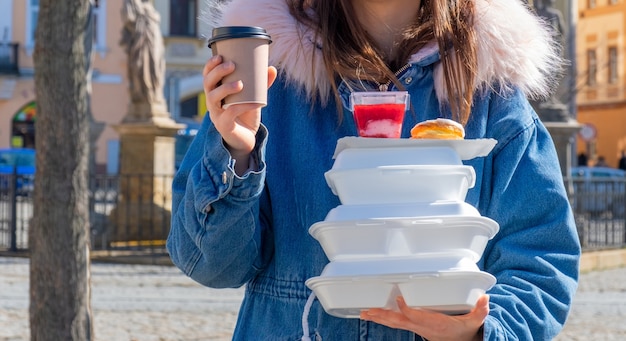 Jonge vrouw op straat met een jas aan met lunchboxen en bezorging van koffie en eten.