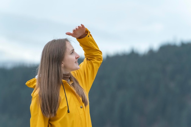 Jonge vrouw op zoek in de verte in gele jas Meisje wandelaar in de natuur Reizen, wandelen en toerisme