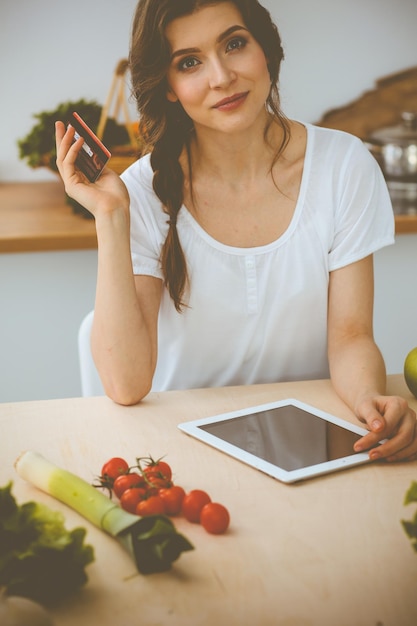 Foto jonge vrouw op zoek naar een nieuw recept voor koken in een keuken. huisvrouw maakt online winkelen via tabletcomputer en creditcard.