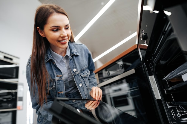 Jonge vrouw op zoek naar nieuwe elektrische oven in een winkelcentrum