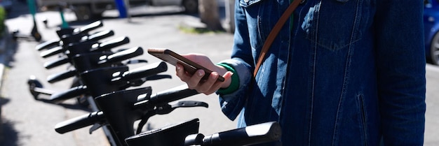 Jonge vrouw opent scooter met behulp van mobiele telefoon-app voor het huren van scooters en fietsen concept