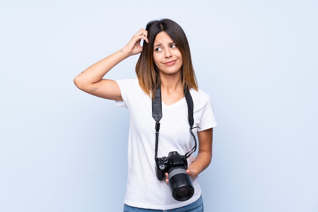 Jonge vrouw over geïsoleerd blauw met een professionele camera en het denken