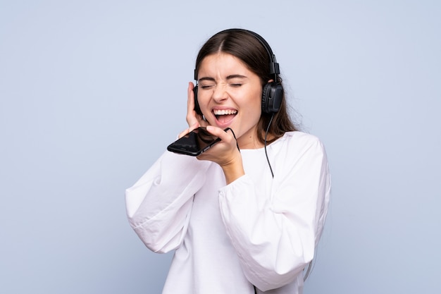 Jonge vrouw over geïsoleerd gebruikend mobiel met hoofdtelefoons en het zingen