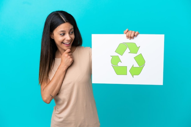 Jonge vrouw over geïsoleerde achtergrond met een bordje met recycle icon