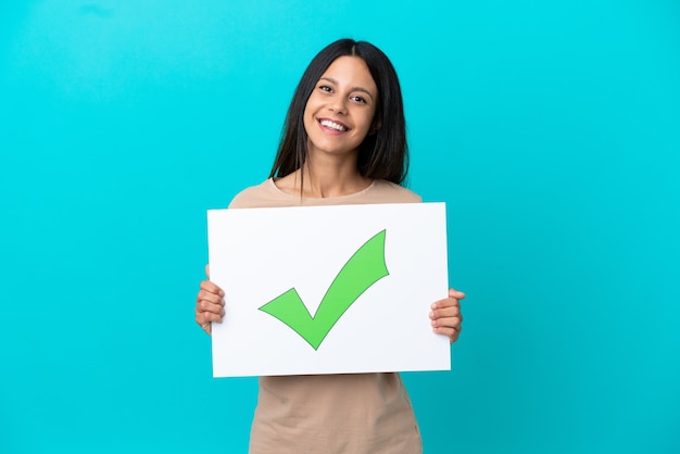 Jonge vrouw over geïsoleerde achtergrond met een bordje met tekst Groen vinkje pictogram met gelukkige expressie