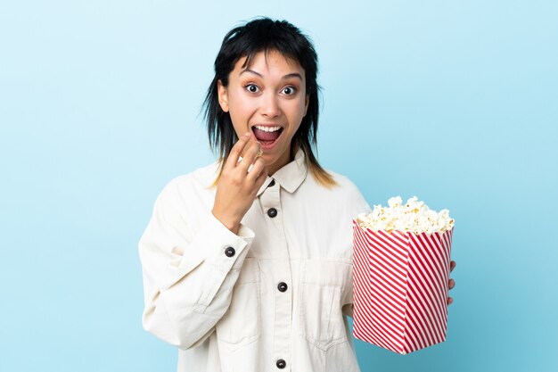 Jonge vrouw over geïsoleerde blauw met een grote emmer popcorns