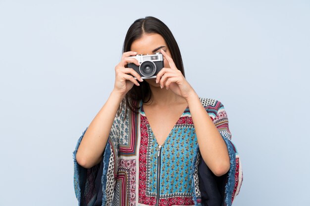 Jonge vrouw over geïsoleerde blauwe muur die een camera houdt