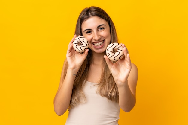 Jonge vrouw over geïsoleerde gele holding donuts met gelukkige uitdrukking