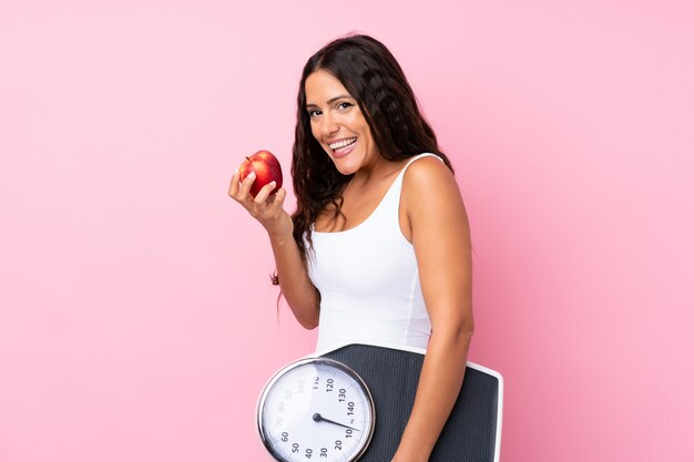 Jonge vrouw over geïsoleerde roze met weegmachine en met een appel