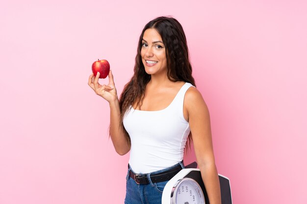 Jonge vrouw over geïsoleerde roze met weegmachine en met een appel