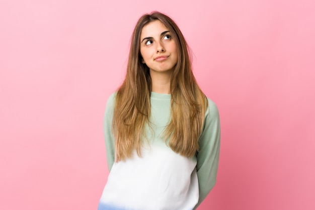 Jonge vrouw over geïsoleerde roze muur en omhoog het kijken