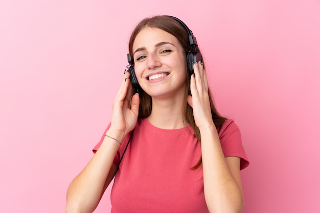 Jonge vrouw over geïsoleerde roze muur het luisteren muziek