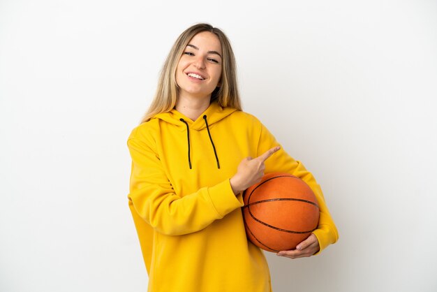 Jonge vrouw over geïsoleerde witte achtergrond die basketbal speelt en naar de laterale wijst