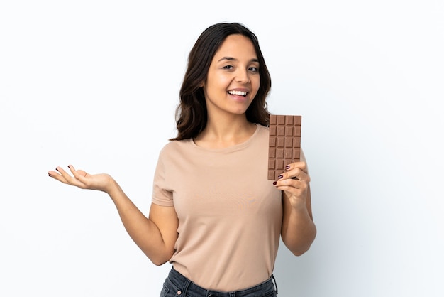 Jonge vrouw over geïsoleerde witte achtergrond die een chocoladetablet nemen en verrast