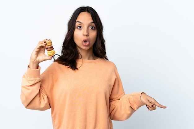 Jonge vrouw over geïsoleerde witte achtergrond die kleurrijke Franse macarons houdt en kant richt