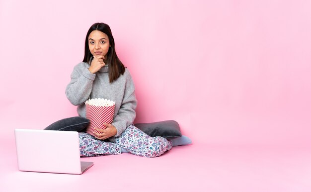 Jonge vrouw popcorn eten tijdens het kijken naar een film op de laptop denken