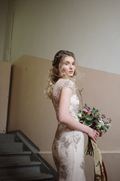 Jonge vrouw poseren in een lichte lange kanten jurk met een boeket bloemen in haar handen