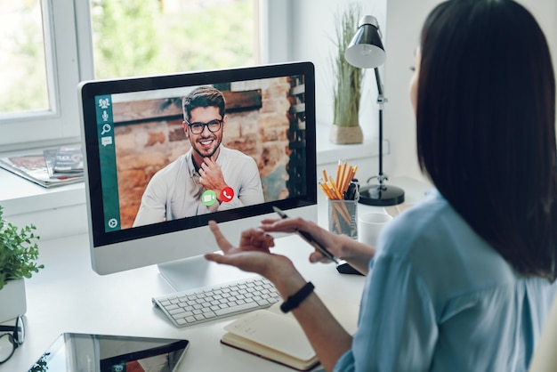 Jonge vrouw praat met collega via videogesprek terwijl ze op kantoor zit