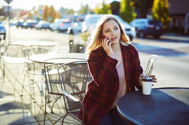 Jonge vrouw praat op de mobiele telefoon terwijl ze op het stoepcafé zit