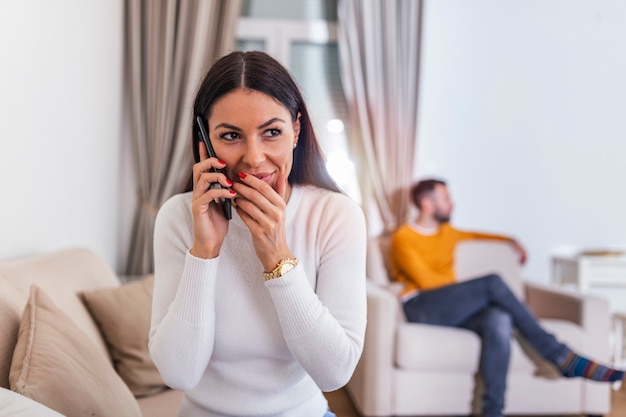 Jonge vrouw praten privé op mobiele telefoon terwijl haar man tv kijkt in de rug.