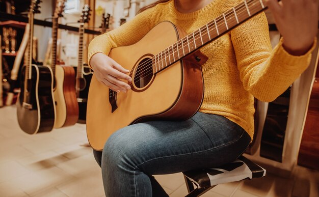 Jonge vrouw probeert en koopt een nieuwe houten gitaar in instrumentale winkel of winkel