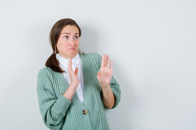 Jonge vrouw probeert zichzelf te blokkeren met handen in blouse, vest en ziet er bang uit, vooraanzicht.