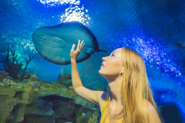 Jonge vrouw raakt een pijlstaartrog aan in een oceanariumtunnel