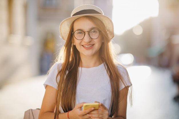 Jonge vrouw reist in hoed en bril staat op straat in de stad en SMS op haar mobiele telefoon.