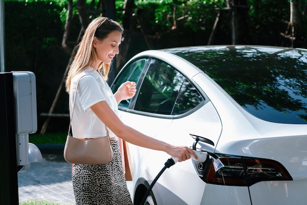 Jonge vrouw reist met elektrische auto's opladen in groene duurzame stad buitentuin in de zomer Stedelijke duurzaamheid levensstijl door groene schone oplaadbare energie van elektrische BEV-voertuigen