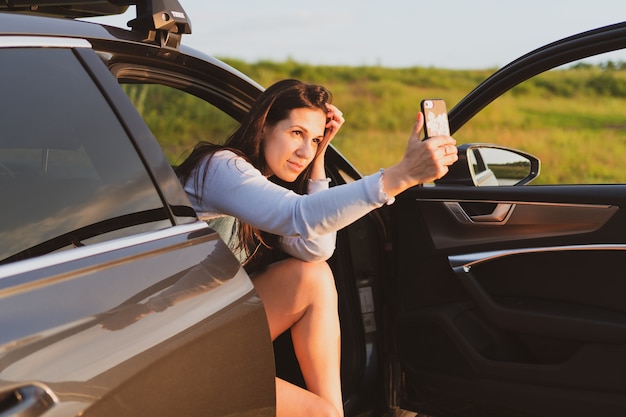 Jonge vrouw reist over de wegen met een auto die langs de kant van de weg is gestopt en foto's maakt met...