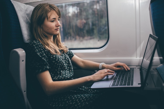 Jonge vrouw reizen in de trein. werken op afstand op laptop tijdens het binnen zitten. student of toerist hebben een kleine reis. bedrijf. typen op toetsenbord.