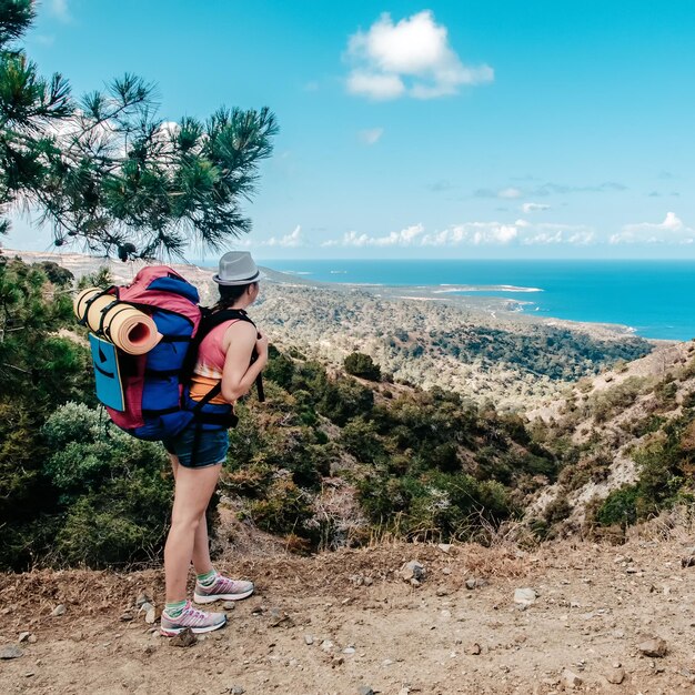 Jonge vrouw reizen meisje met rugzak wandelingen op prachtige landschap achtergrond zee en heuvels Kaap van Aphrodite Cyprus populaire bestemming voor zomervakantie