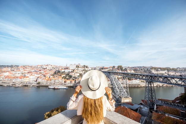 Jonge vrouw reiziger in zonnehoed staande op de prachtige luchtfoto stadsgezicht achtergrond met Douro rivier en Luise brug tijdens het ochtendlicht in Porto, Portugal