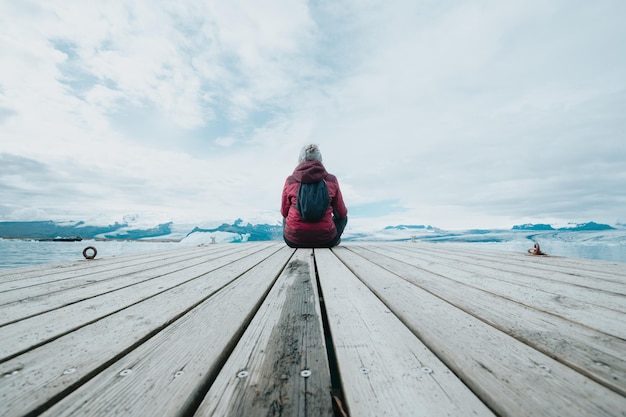 Jonge vrouw reiziger terug geschoten zittend op de dokken ontspannen en denken voor de gletsjers van Jokulsarlon in IJsland Ruimte kopiëren Leef je droom liefde in IJsland road trip stijl