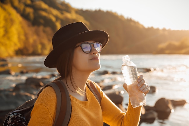 Jonge vrouw reiziger zuiver water drinken uit fles op natuur rivier achtergrond bottle