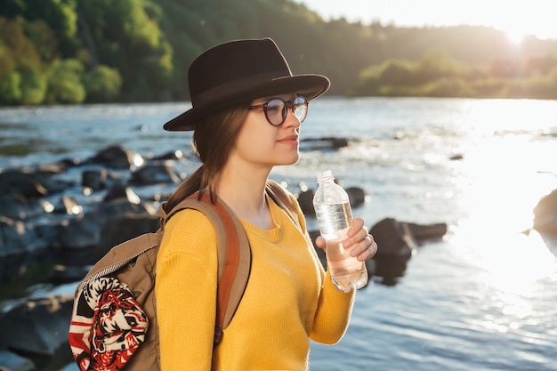 Jonge vrouw reiziger zuiver water drinken uit fles op natuur rivier achtergrond bottle