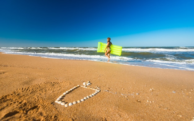 Jonge vrouw rent langs het strand met een luchtbed langs een cocktailfiguur die op het zandstrand ligt