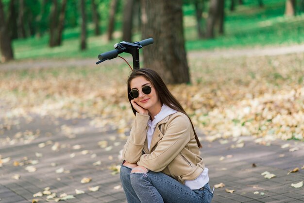 Jonge vrouw rijdt op een elektrische scooter in een herfstpark. Groen vervoer, fileproblemen.