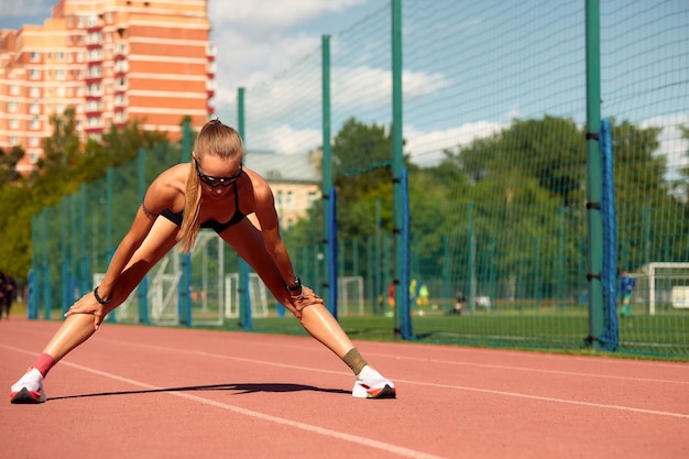 Jonge vrouw runner aan het opwarmen op het circuit Fit runner training rekt haar spieren en warmt op op het circuit