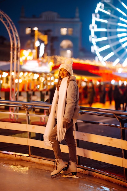 Jonge vrouw schaatsen op een ijsbaan in een feestelijke kerstmarkt in de avond. Lichten rond.