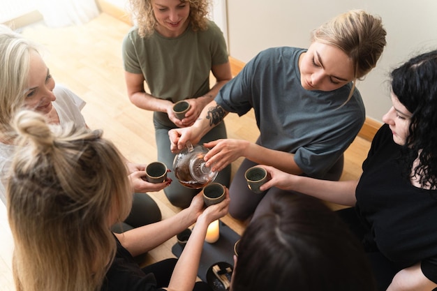 Jonge vrouw schenkt hete thee in voor haar vrienden die rond een dienblad zitten tijdens een theeceremonie