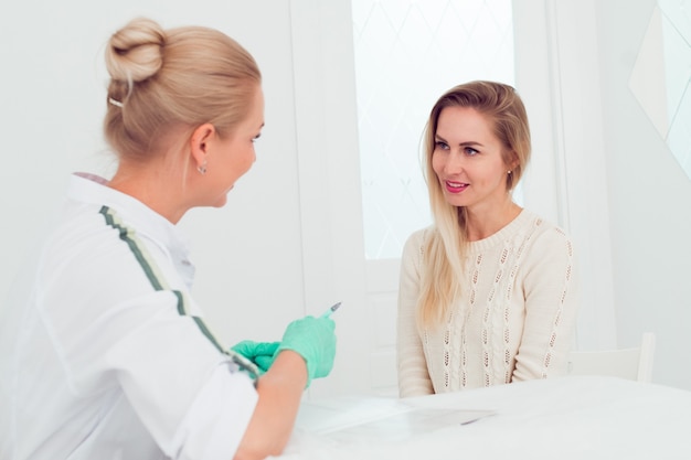 Foto jonge vrouw schoonheidsspecialiste praten met een jonge blonde vrouw over nieuwe gezichtsverzorging procedures profe